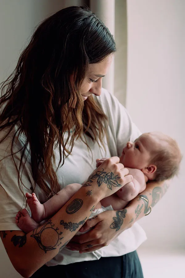 Frau mit braunen Haaren und weißem T-Shirt hält Baby in den armen.